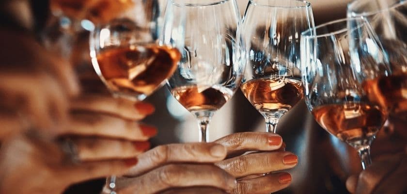 Close-up of several people holding and clinking glasses of rosé wine, with hands and glass stems in focus against a softly blurred background.