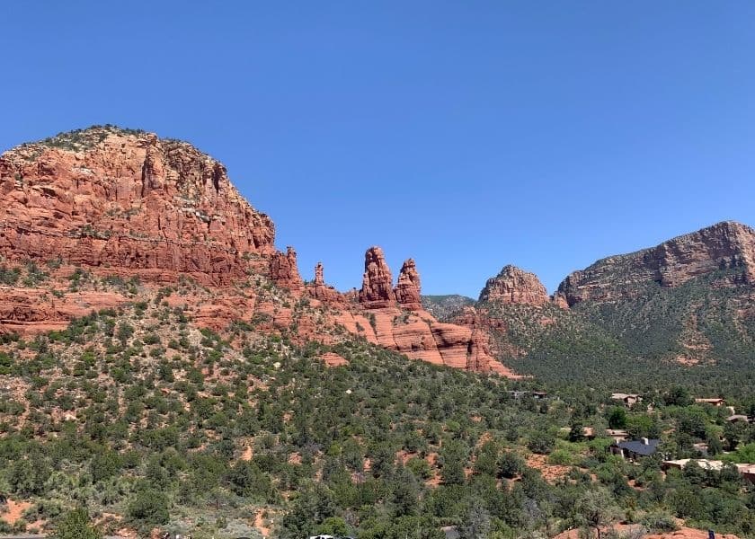 red rock formations rising above a green desert landscape under a clear blue sky